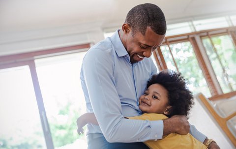 Portrait of american african father and son hugging laughing in living room. Happy daddy and his little boy spending leisure time at home